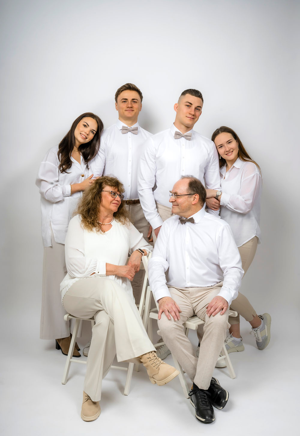 Familienfoto zu sechst mit Söhnen und Schwiegertöchtern. Alle in weiss und beige gekleidet und fotografiert vor weissem Hintegrund bei uns im Fotostudio in Weinheim.