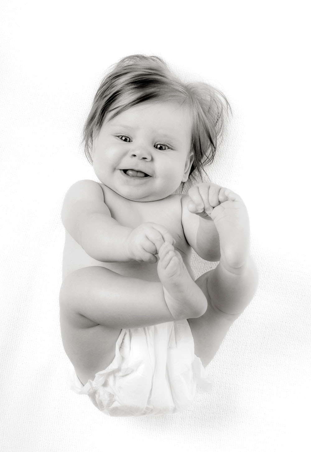 Bei einem Newbornshooting entstand dieses Babyfoto in Schwarzweiss. Baby liegt auf dem Rücken und spielt mit seinen Füßchen. Fotografiert wurde dieses Neugeborenenfoto bei uns im Fotostudio in Weinheim